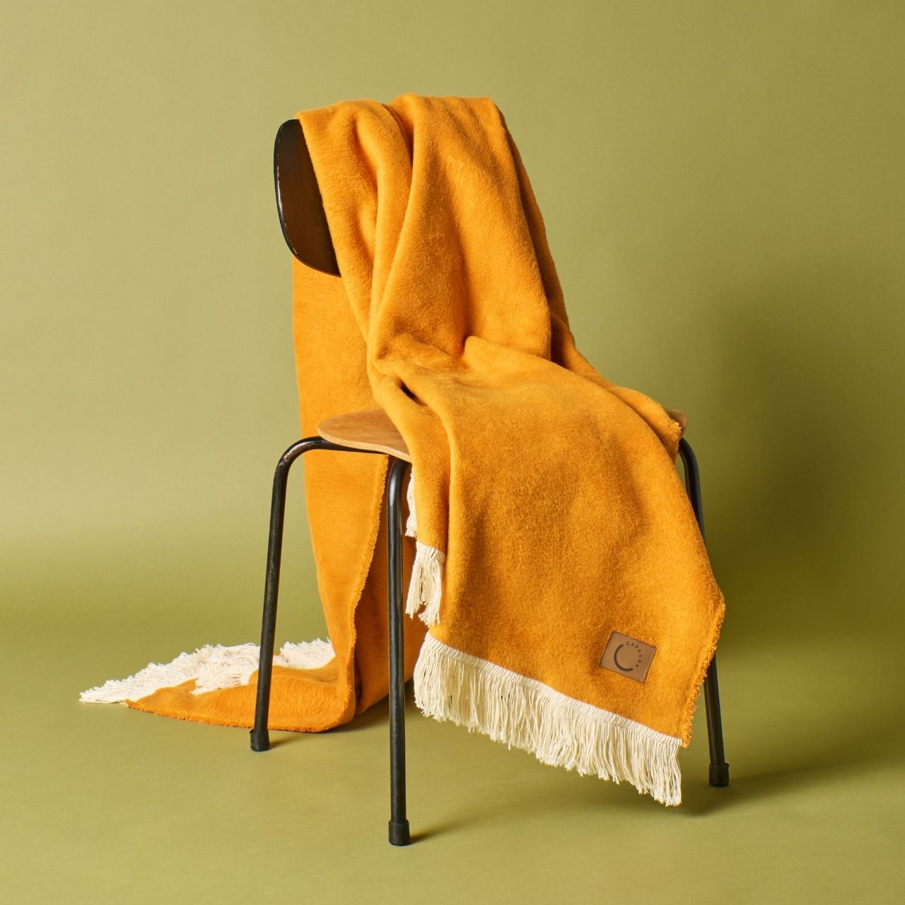 Kuscheldecke aus Baumwolle mit Fransen in Ockerorange (Stuhlansicht)